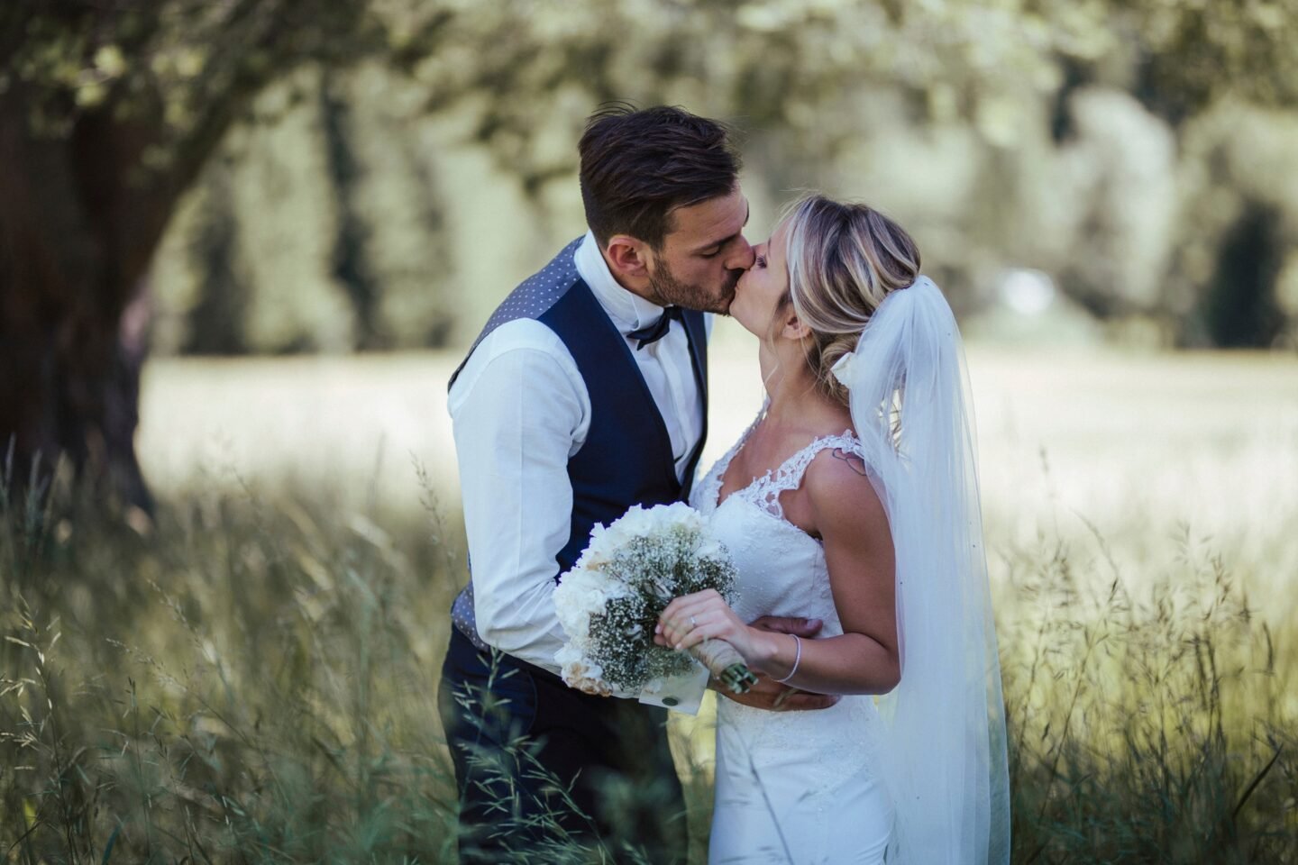 Bride and groom sharing a kiss on their wedding day amidst a serene natural backdrop.